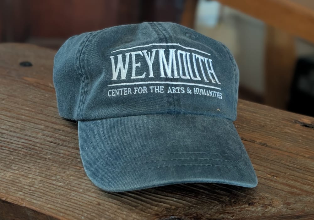Just an image of a baseball cap sitting on a table. The hat is embossed with the Weymouth logo.